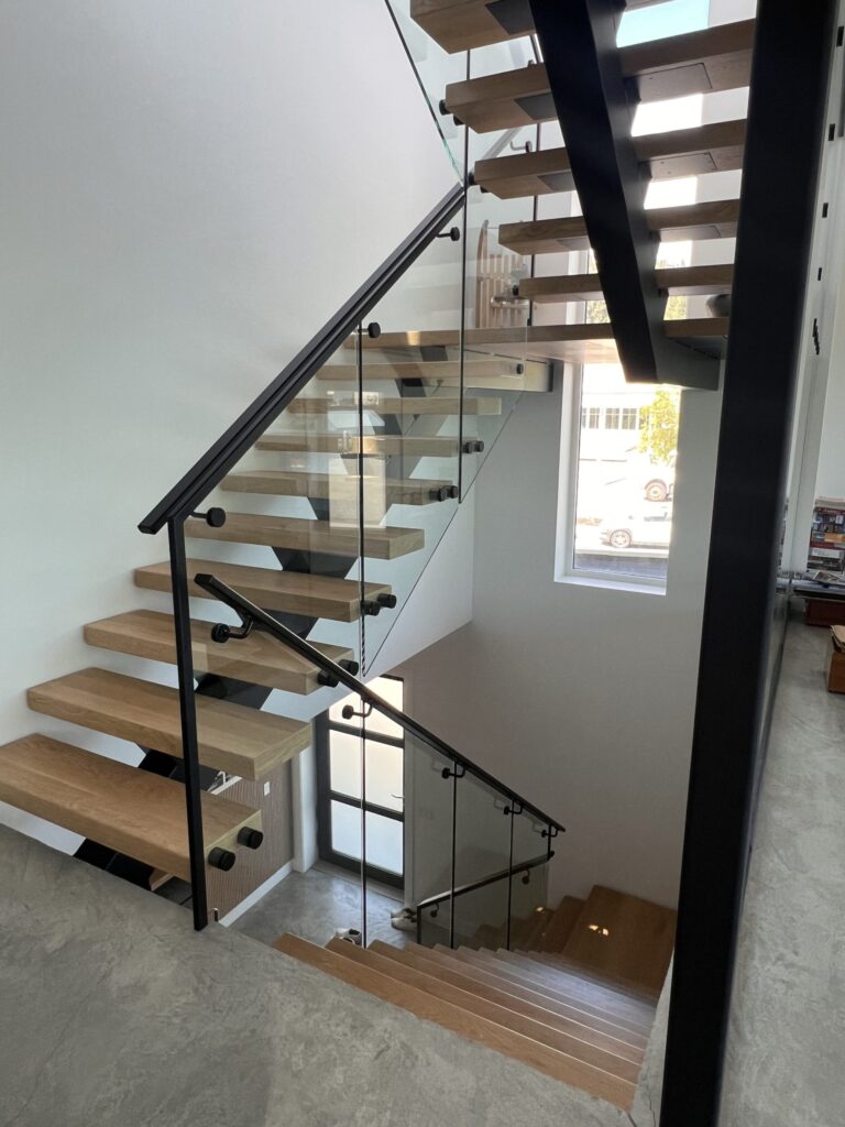 3 Story Floating Mono Stringer Stair with an Open Rise and 3" Treads. 12mm Glass Railing with black metal top rail and black metal handrail U-shaped staircase