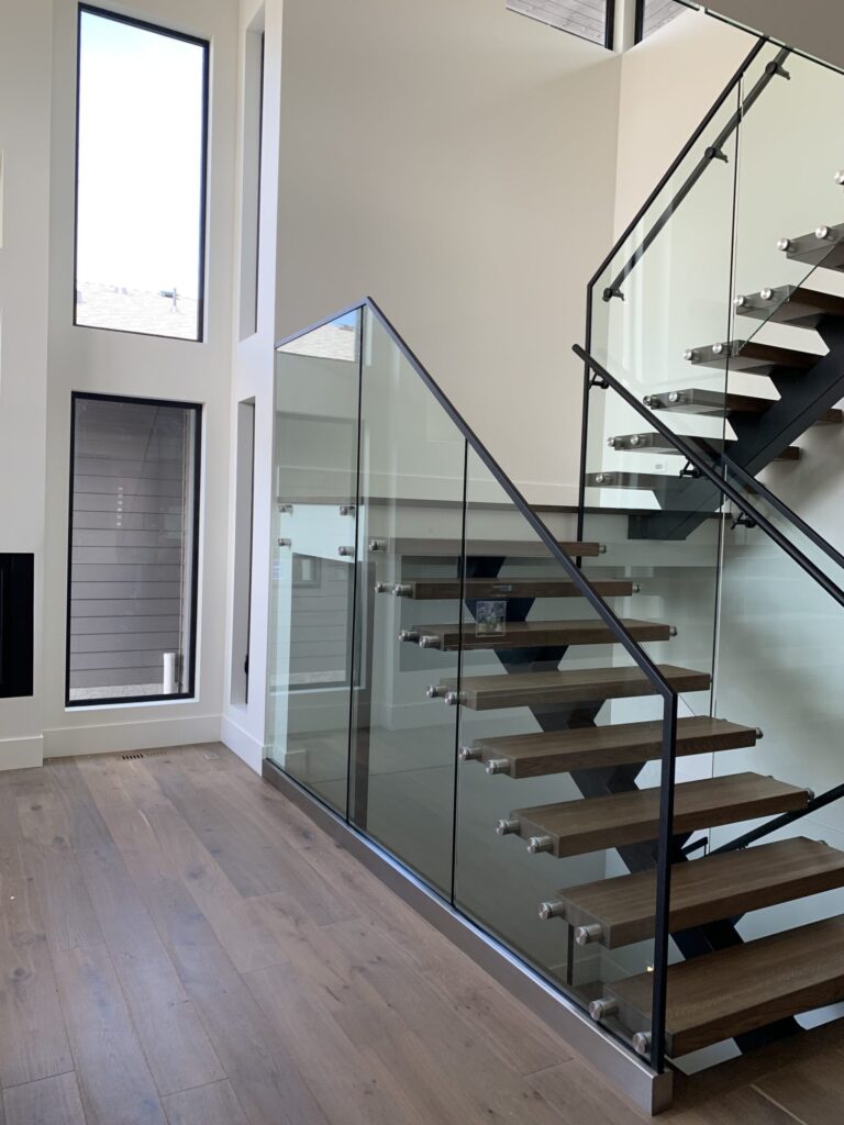Floating Black Metal Mono Stringer Staircase with an Open Rise and 3" Wood Treads and 12mm Glass Railing, Black metal top rail and Standoffs. U-Shaped
