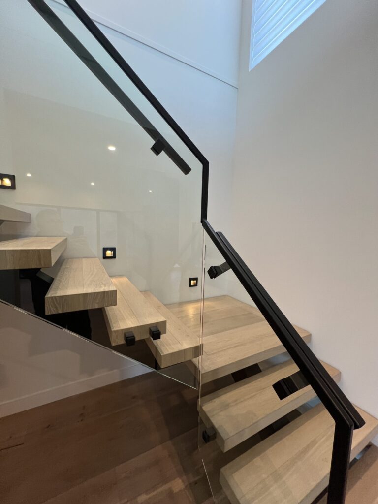 Two story interior mono stringer stairway with 12mm glass railing and black metal top and hand rail